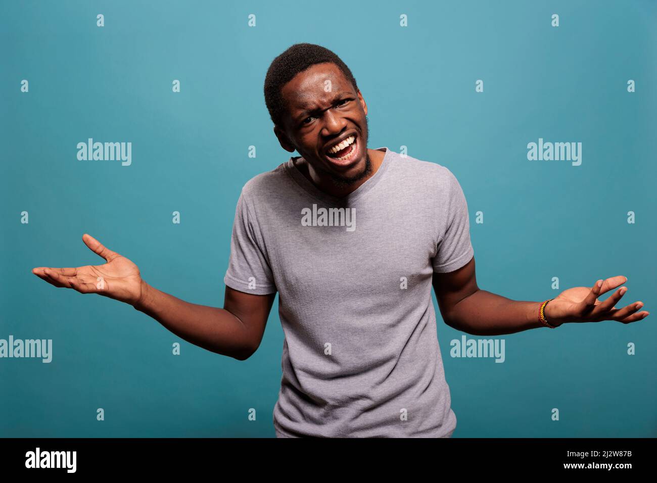 Upset man doing i dont know symbol in front of camera, expressing confusion and being unsure about decision. Person feeling angry about ambiguous question, having doubtful reaction. Stock Photo