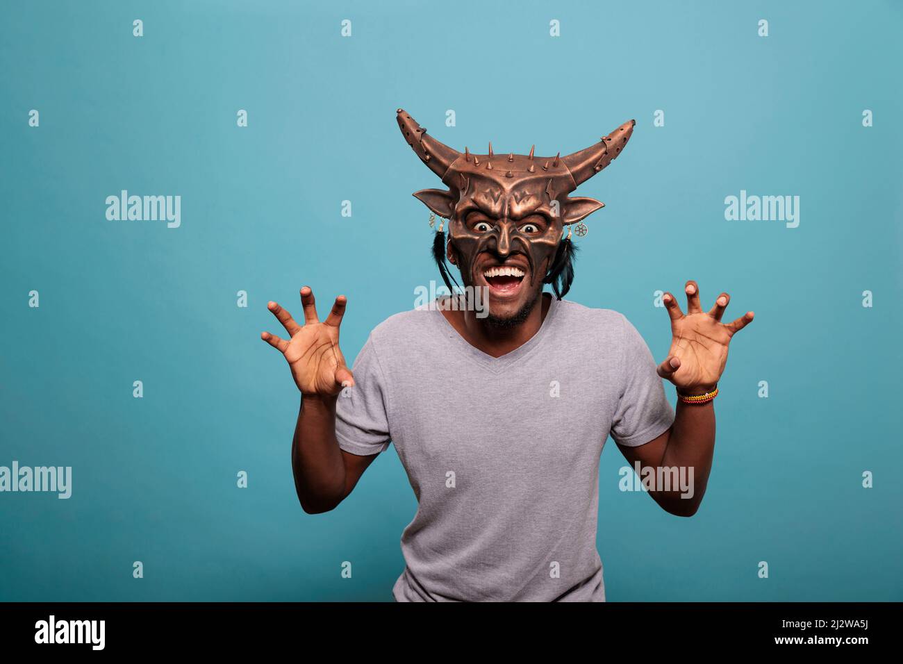 Young person wearing traditional indigenous face mask used in shaman culture and history to create native tribal ritual. Man using traditional tribe art and cultural object for entertainment. Stock Photo