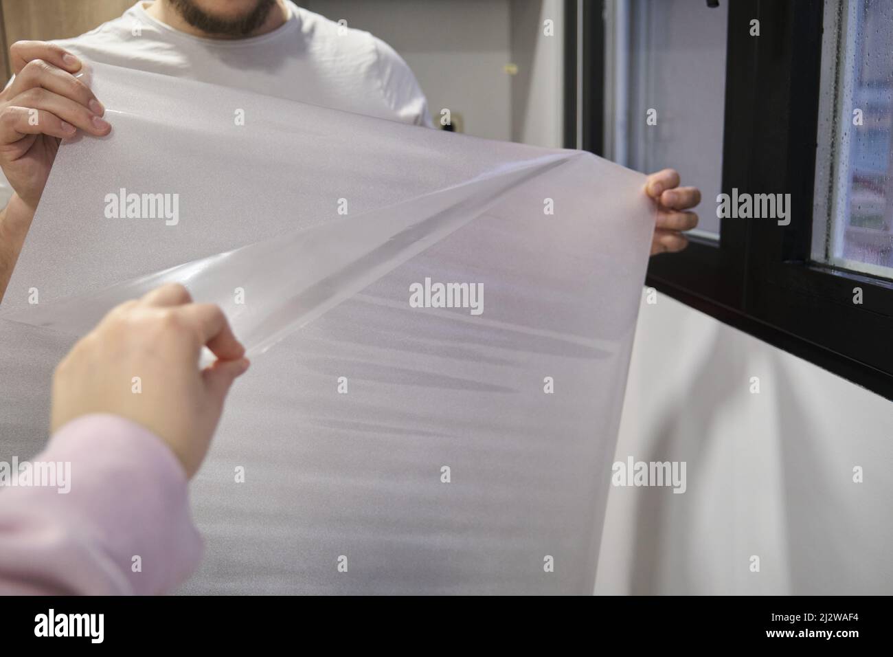 Man taking off the plastic to install frosted window vinyl on the window glass. Stock Photo