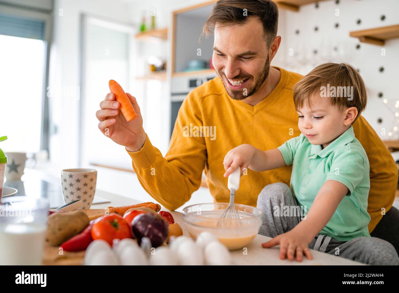 Happy single father with a toddler boy having fun and preparing healthy food in kitchen at home. Stock Photo