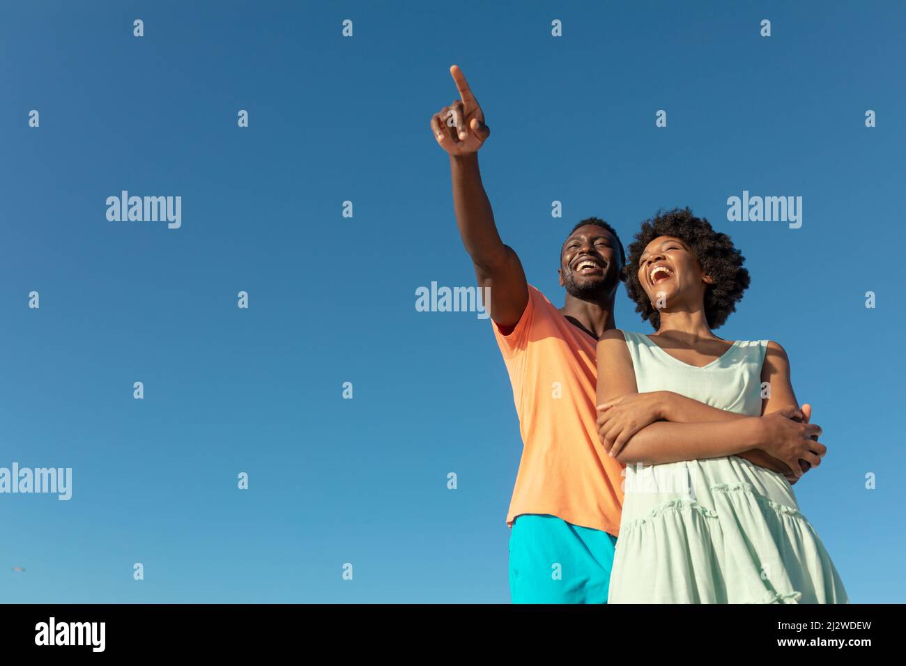 Low angle view of happy african american man pointing with girlfriend against clear blue sky Stock Photo
