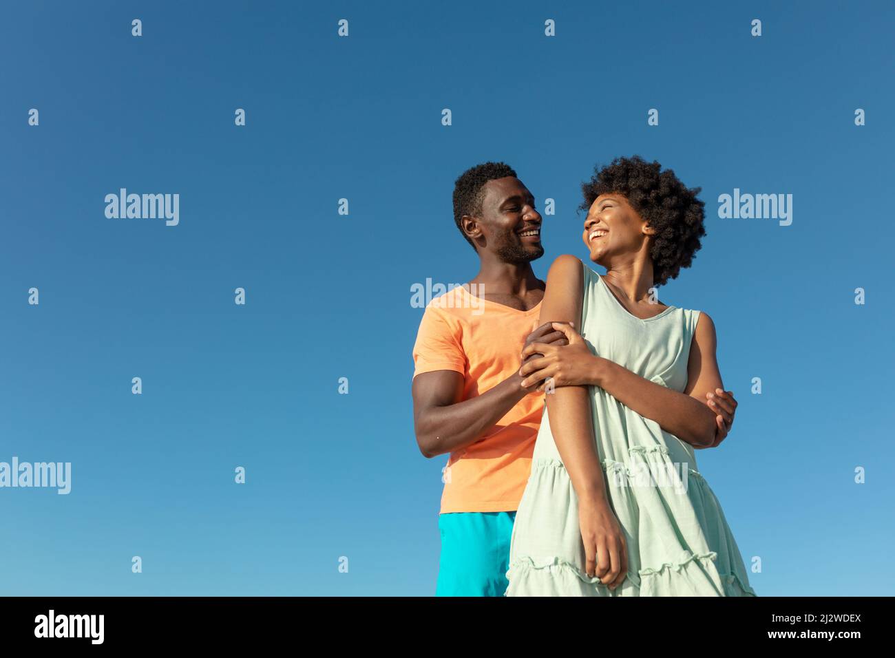 Low angle view of smiling african american couple against clear blue sky with copy space Stock Photo