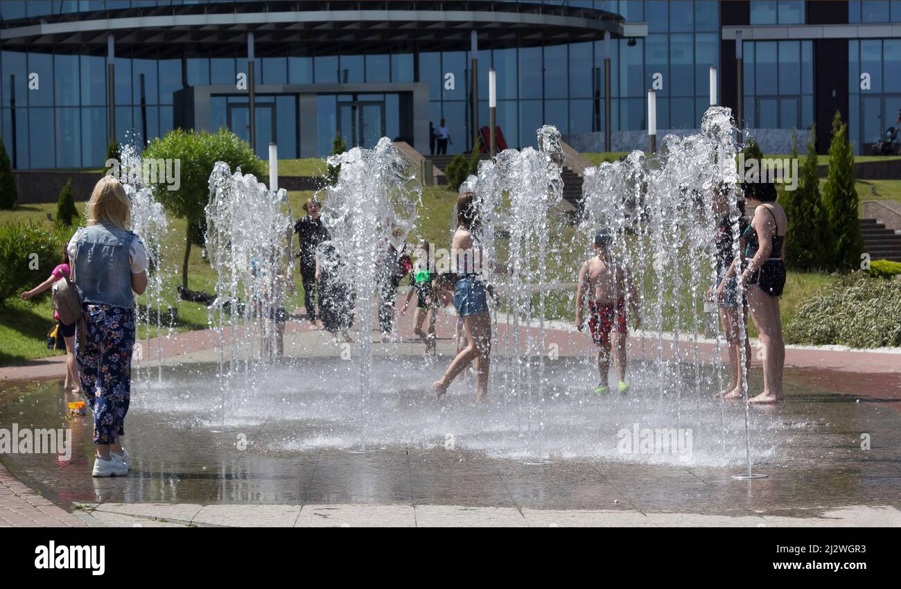 Minsk, Belarus 08.06.2020. Children frolic in a dry fountain on a hot summer day. The boys run among the jets of a working fountain. Stock Photo