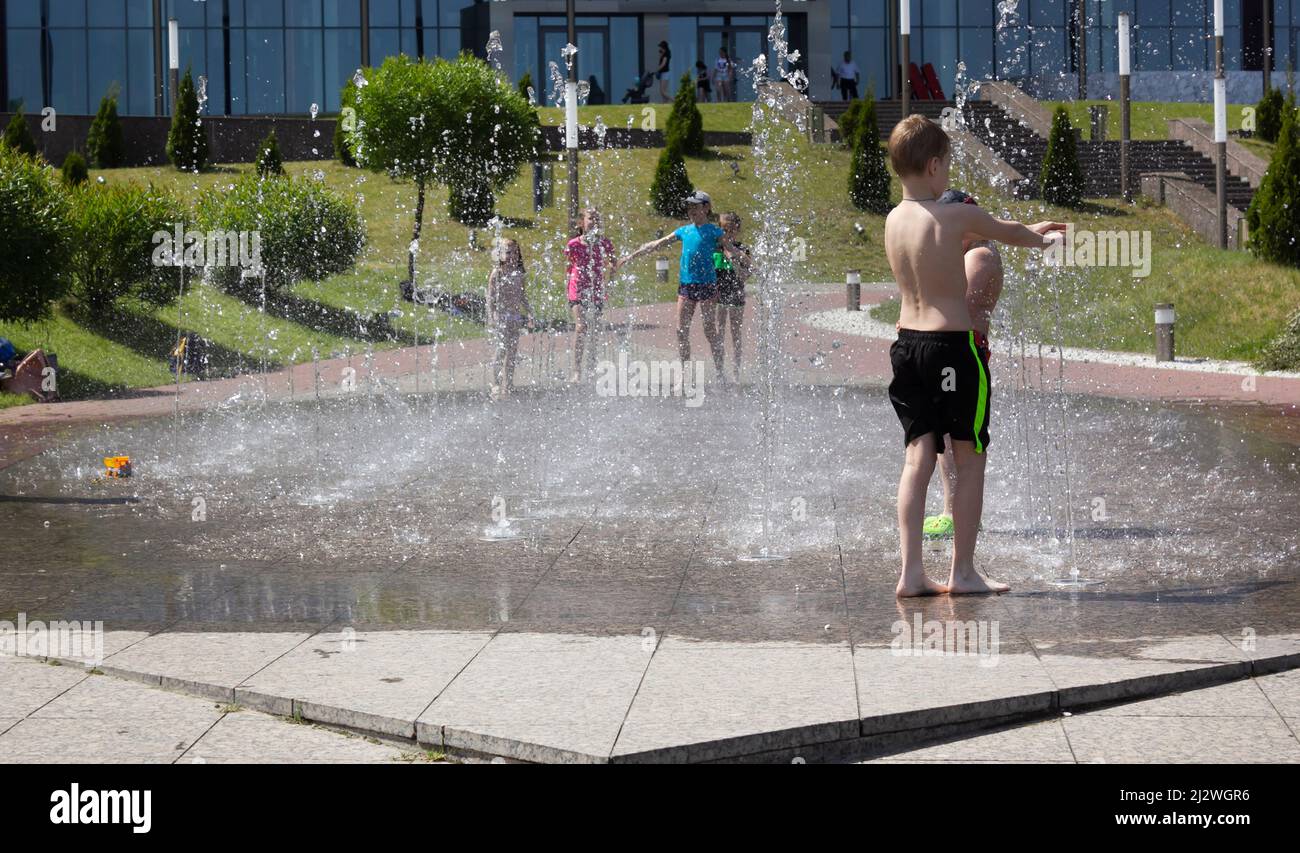 Minsk, Belarus 08.06.2020. Children frolic in a dry fountain on a hot summer day. The boys run among the jets of a working fountain. Stock Photo