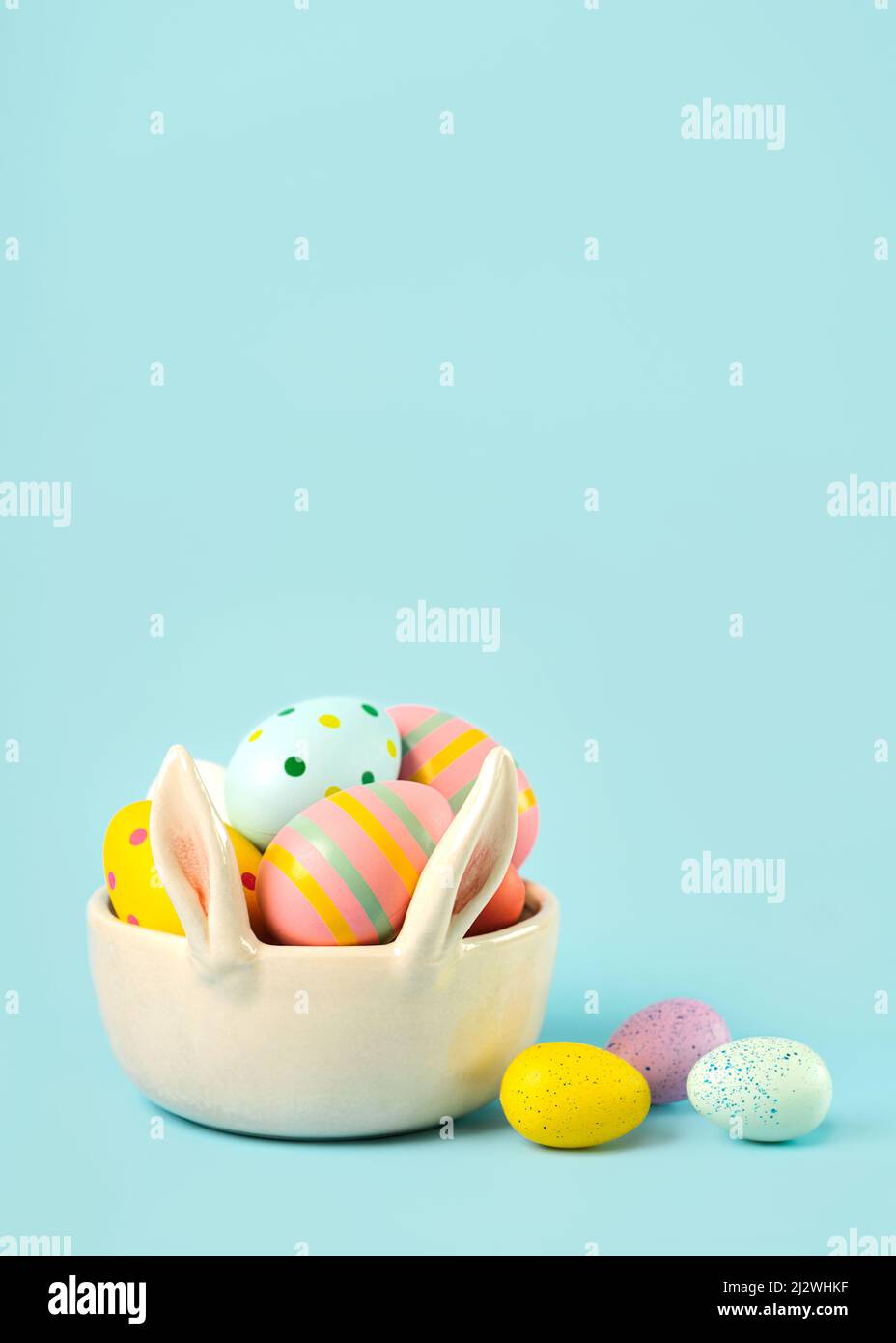 Happy Easter. Colored easter painted eggs in a bunny ears bowl with copy space over blue background Stock Photo