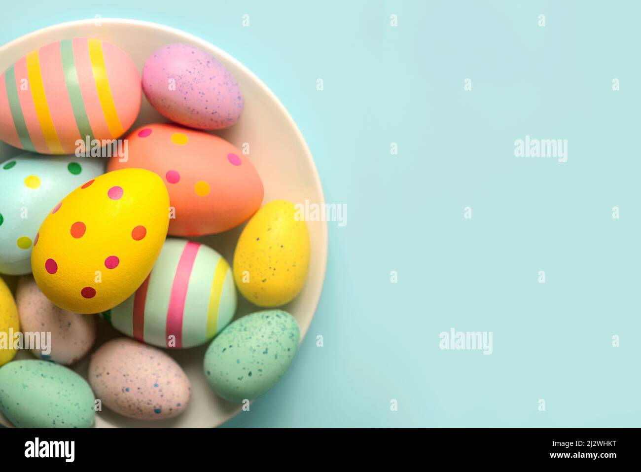 Happy Easter. Colored easter painted eggs in a bowl with copy space over blue background Stock Photo