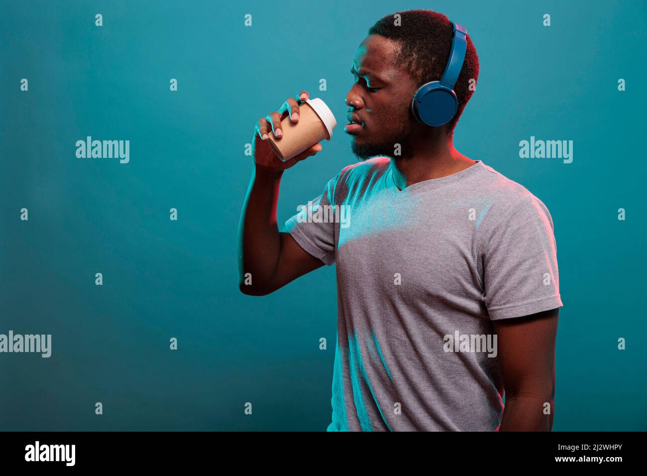 Carefree guy listening to music on headset and drinking coffee from cup to  relax in studio. Confident adult with wireless headphones enjoying drink  and mp3 sound on audio gadget Stock Photo -