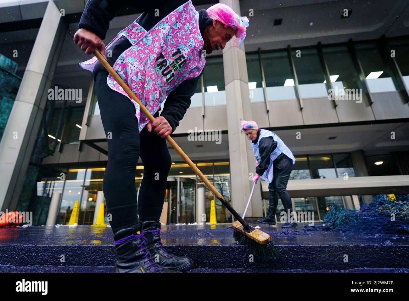 Ocean Rebellion activists sweep up fake oil during a demonstration outside the International Maritime Organisation (IMO) in central London. Picture date: Monday April 4, 2022. Stock Photo
