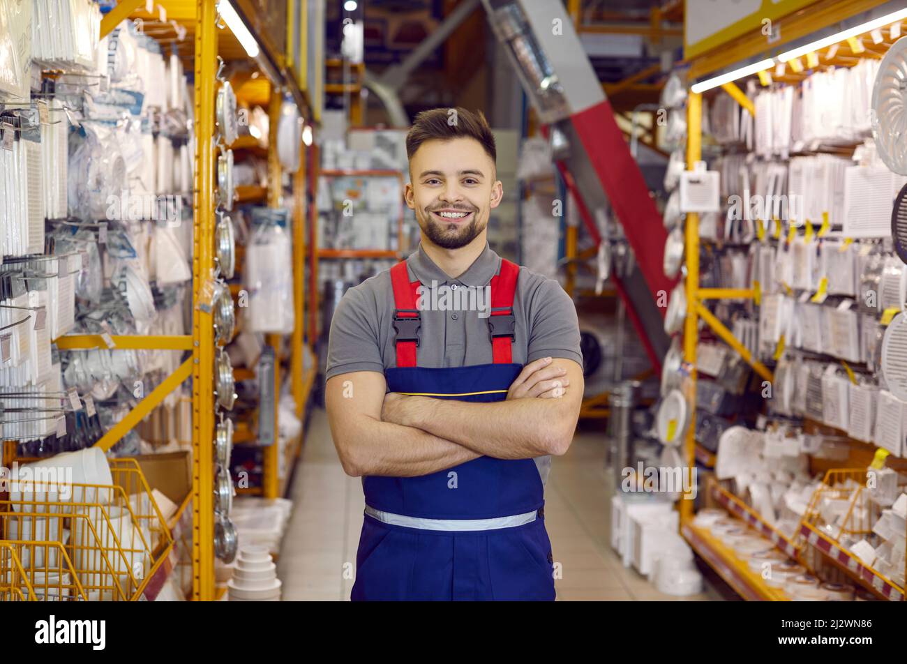 Salesman in uniform at hardware store. Man standing next to shelves with tools, smiling Stock Photo