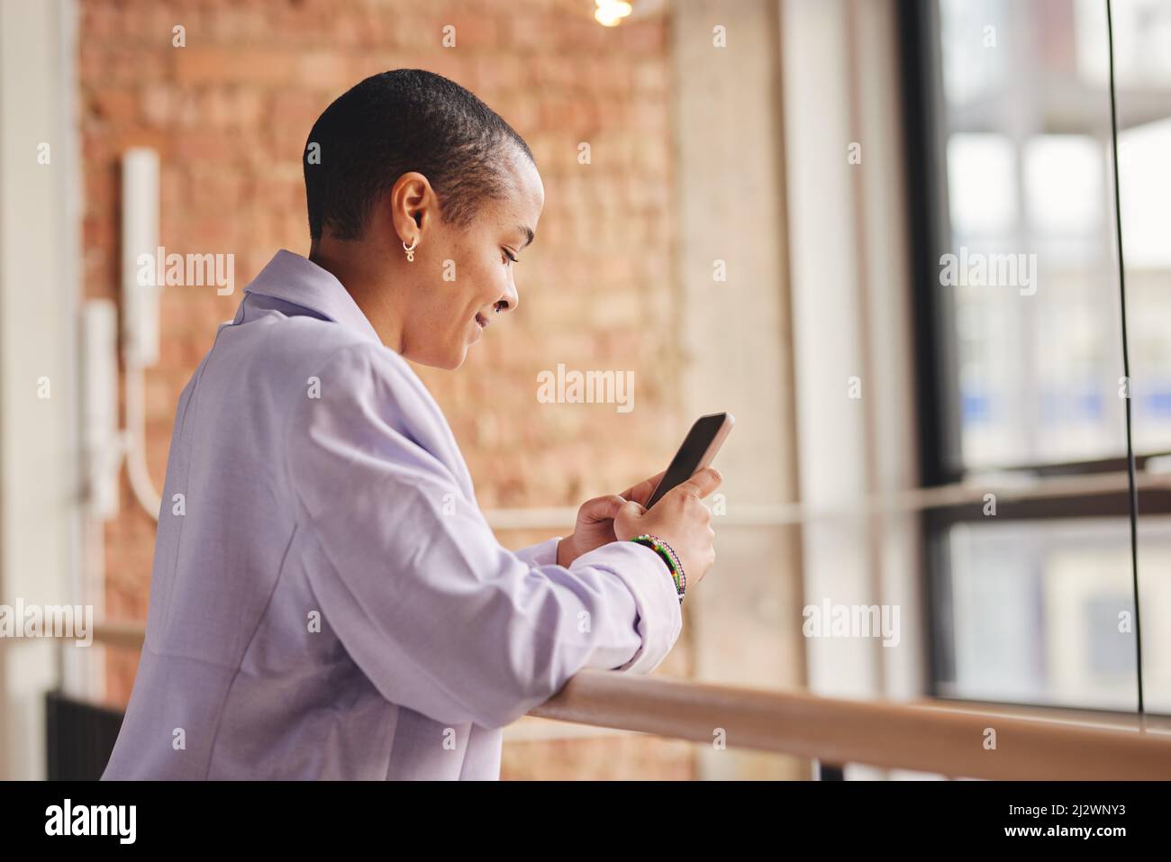Portrait of cheerful multiracial LGBTQ mid adult woman leaning on railing and using smartphone Stock Photo