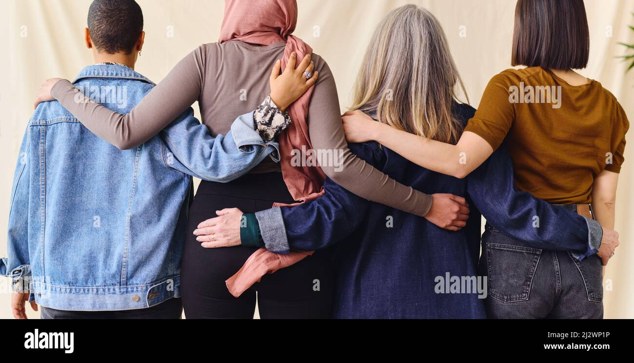 International Women's Day rear view portrait of four women standing with arms around each other in solidarity Stock Photo