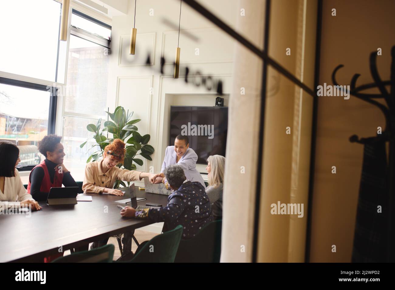 View through window of multiethnic businesswomen fist bumping and smiling in meting room Stock Photo