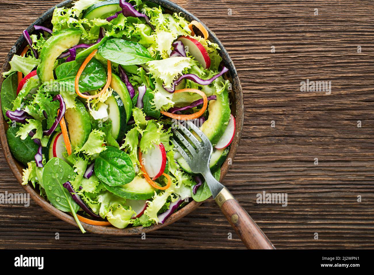 Green lettuce salad meal with avocado and fresh mixed vegetables on wooden table background Stock Photo