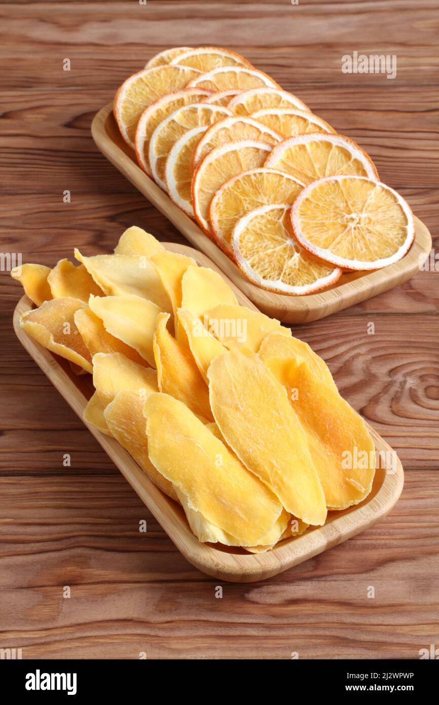 Dried pieces of mango and orange on a bamboo plates on a wooden table. Macro. Closeup. Stock Photo