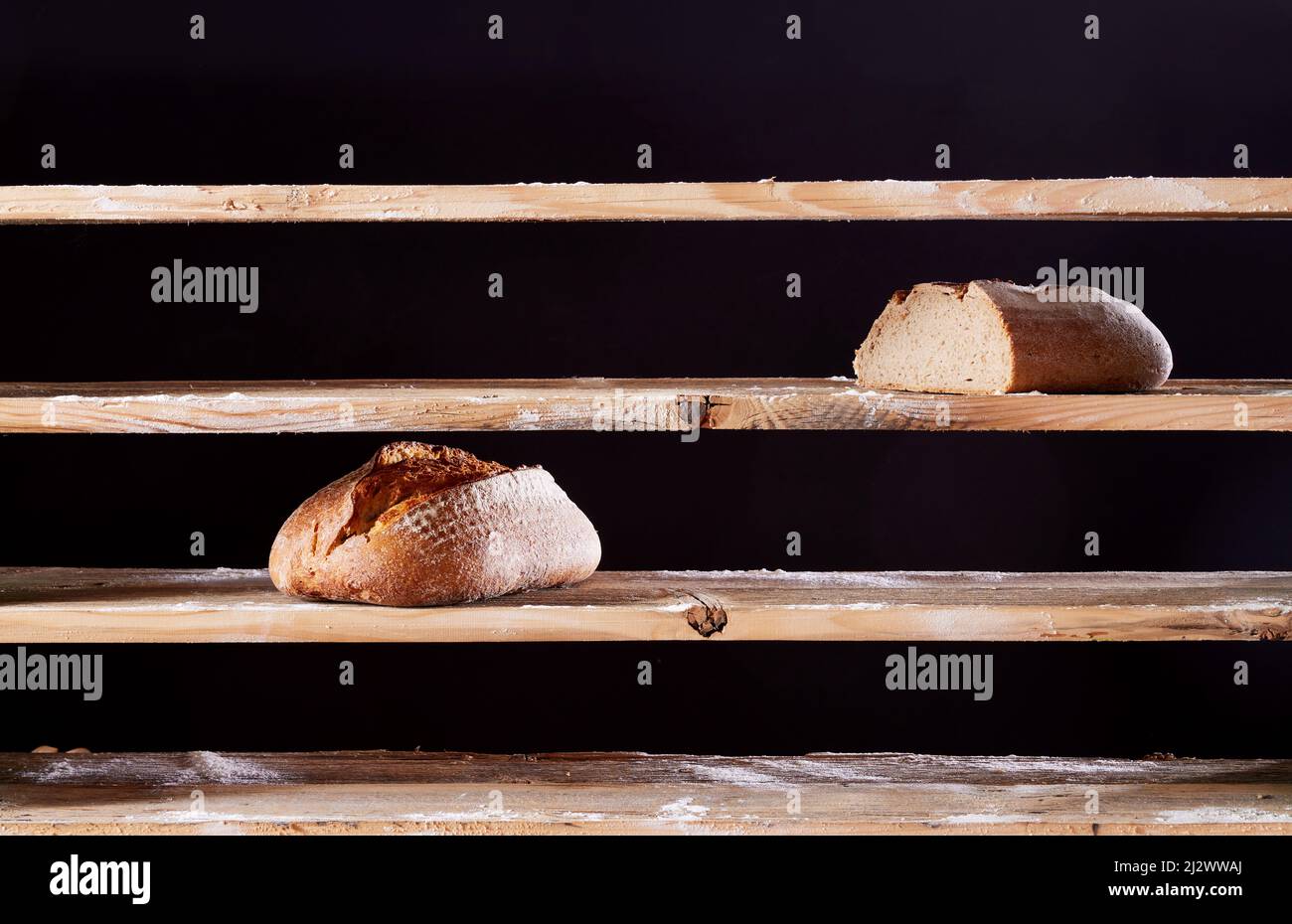 Two baked loaves of bread placed on empty wooden shelves with flour of ...