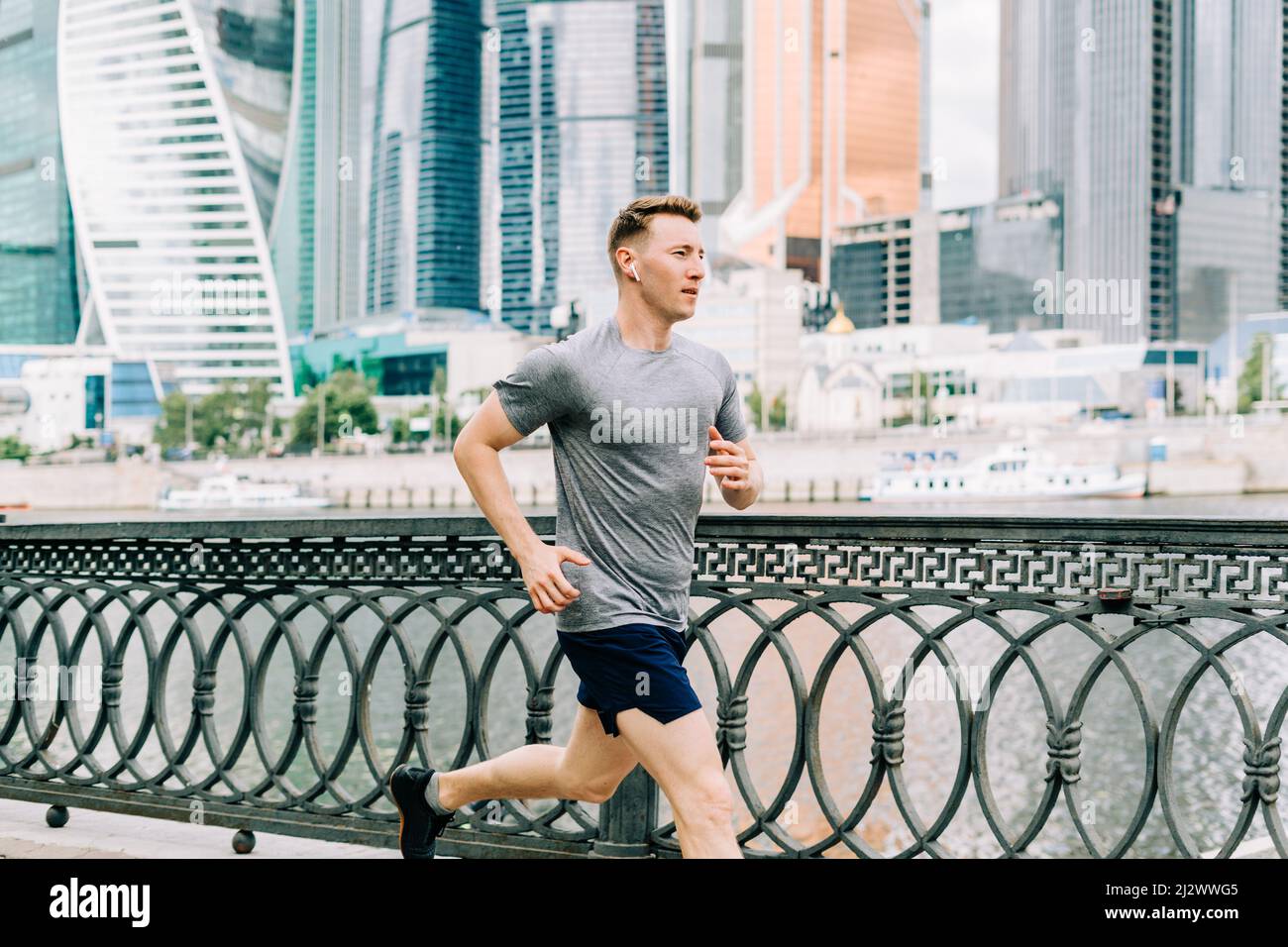 Young athlete man runner running at summer morning, background urban city street. Sports training. Fitness cardio workout in fresh air, jogging Stock Photo