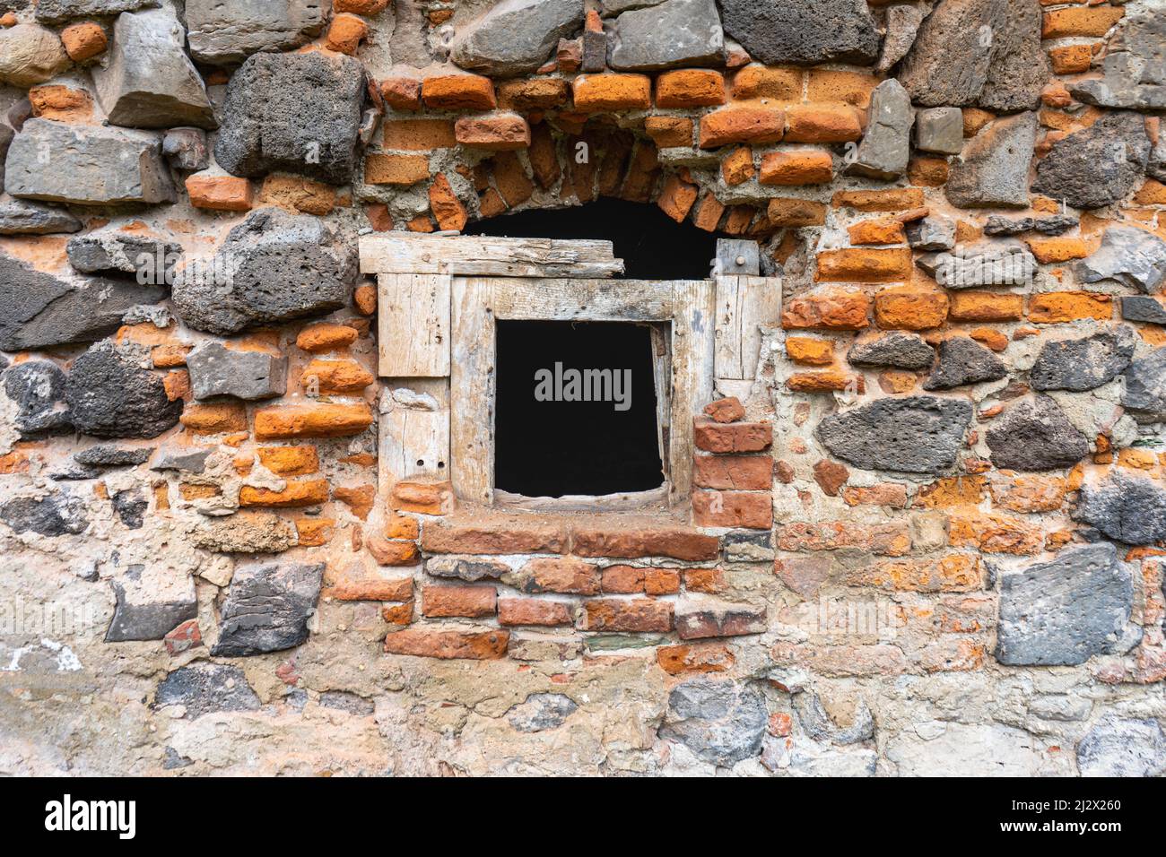 Old window in a wall made of volcanic stone ad bricks Stock Photo
