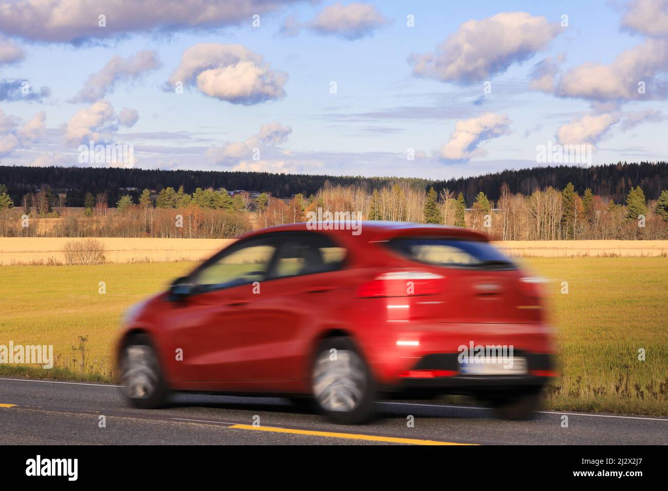 Red car at speed on road on a beautiful day of autumn, side view, in-camera motion blur. Stock Photo