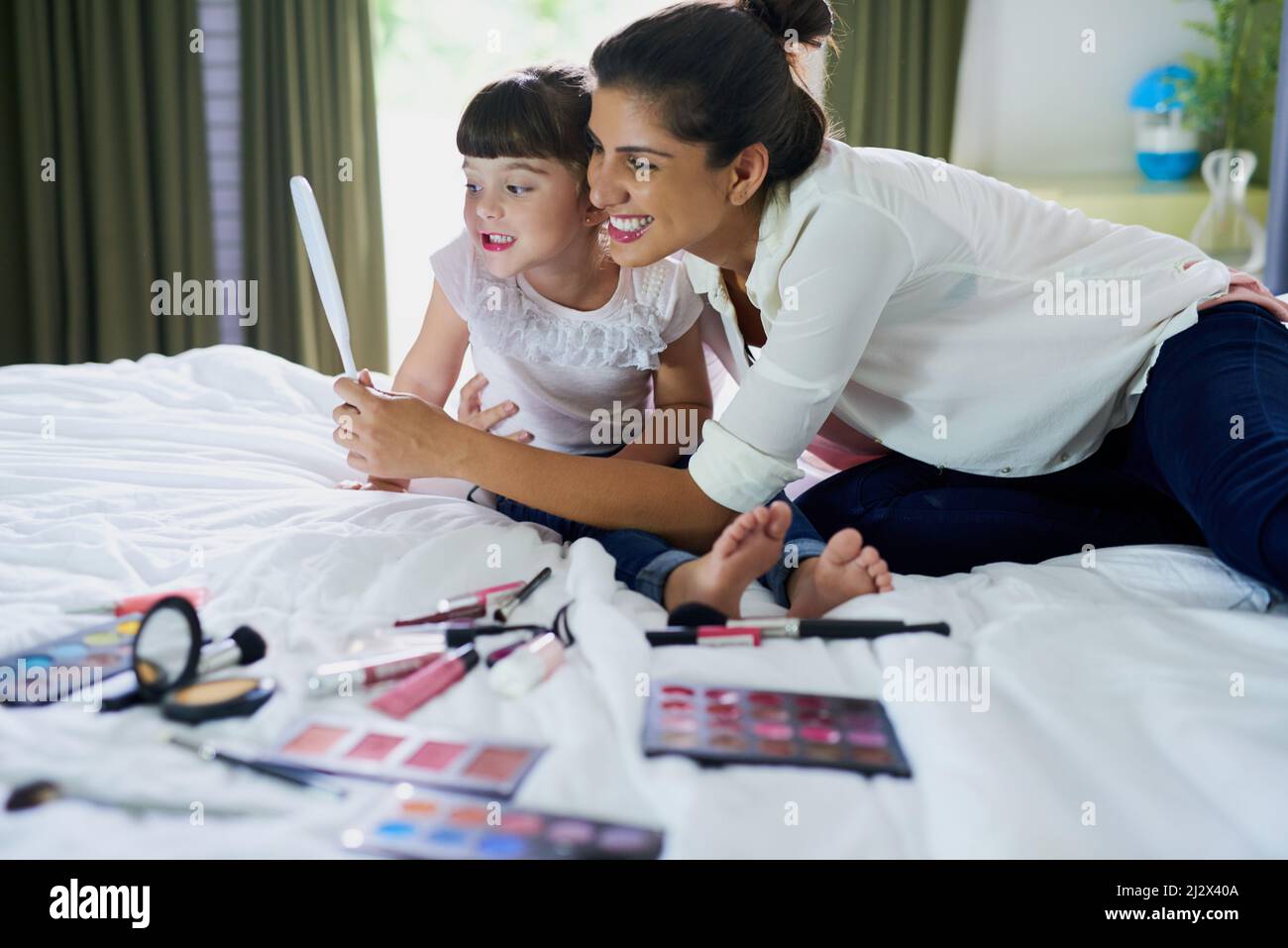 We look so pretty. Shot of a mother and her little daughter playing with makeup on the bed at home. Stock Photo