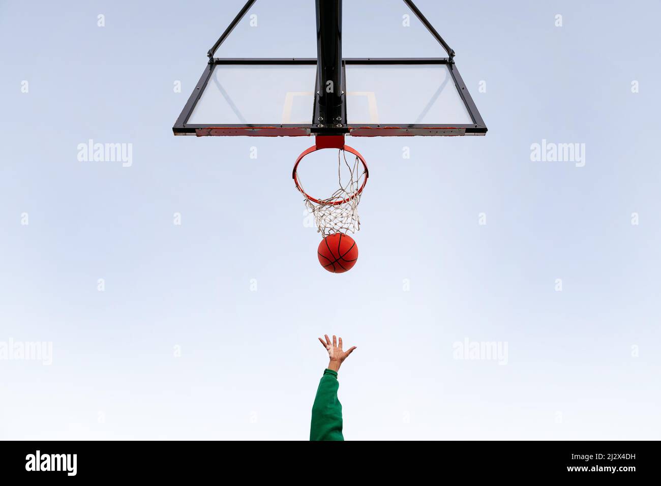 hand shooting in a basketball hoop seen from below with the sky in the background, concept of urban sport outdoors, copy space for text Stock Photo