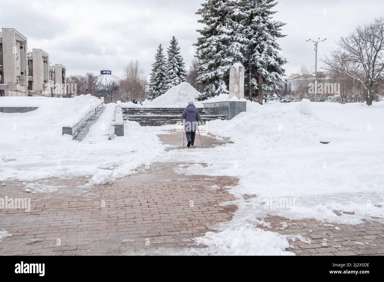 An elderly woman with canes in her hands walks along a snow-covered ...