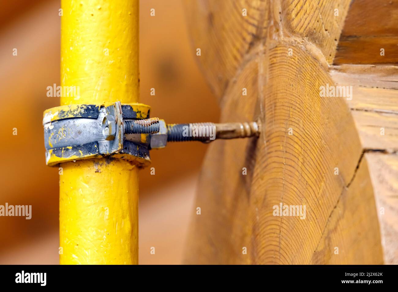 Yellow gas pipe is attached by pipe clamp to wall of log house Stock Photo