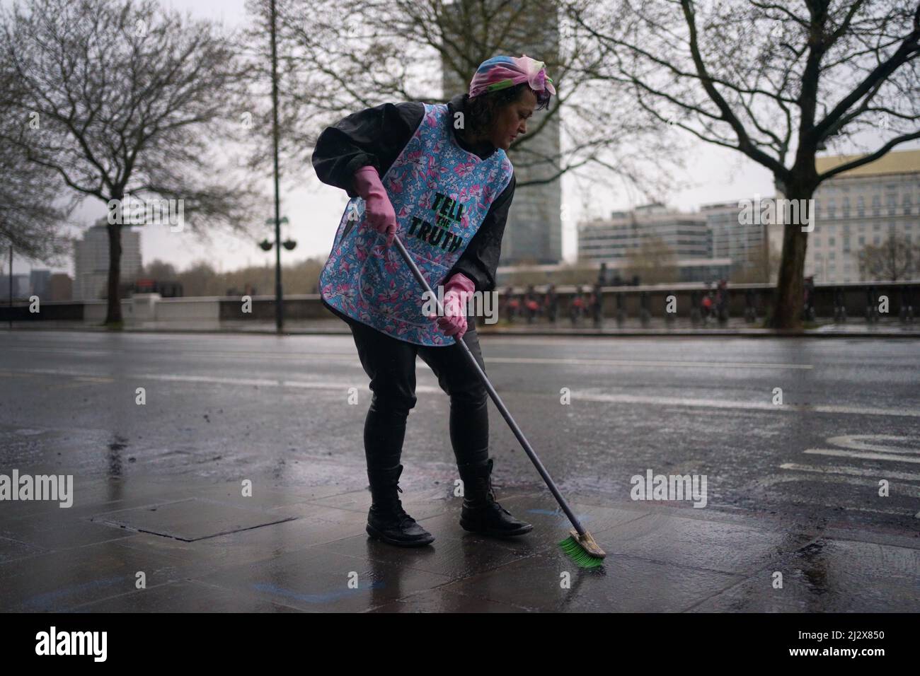 An Ocean Rebellion activist sweeps up fake oil during a demonstration outside the International Maritime Organisation (IMO) in central London. Picture date: Monday April 4, 2022. Stock Photo