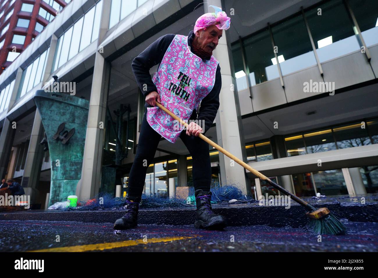 An Ocean Rebellion activist sweeps up fake oil during a demonstration outside the International Maritime Organisation (IMO) in central London. Picture date: Monday April 4, 2022. Stock Photo