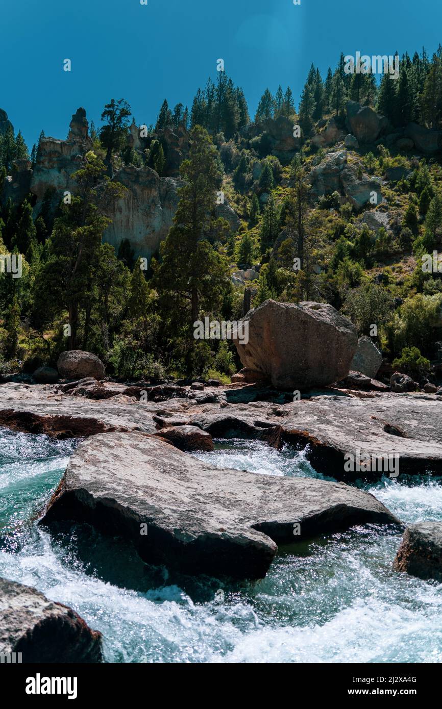 A vertical of a river flowing through rocky banks against mountains ...