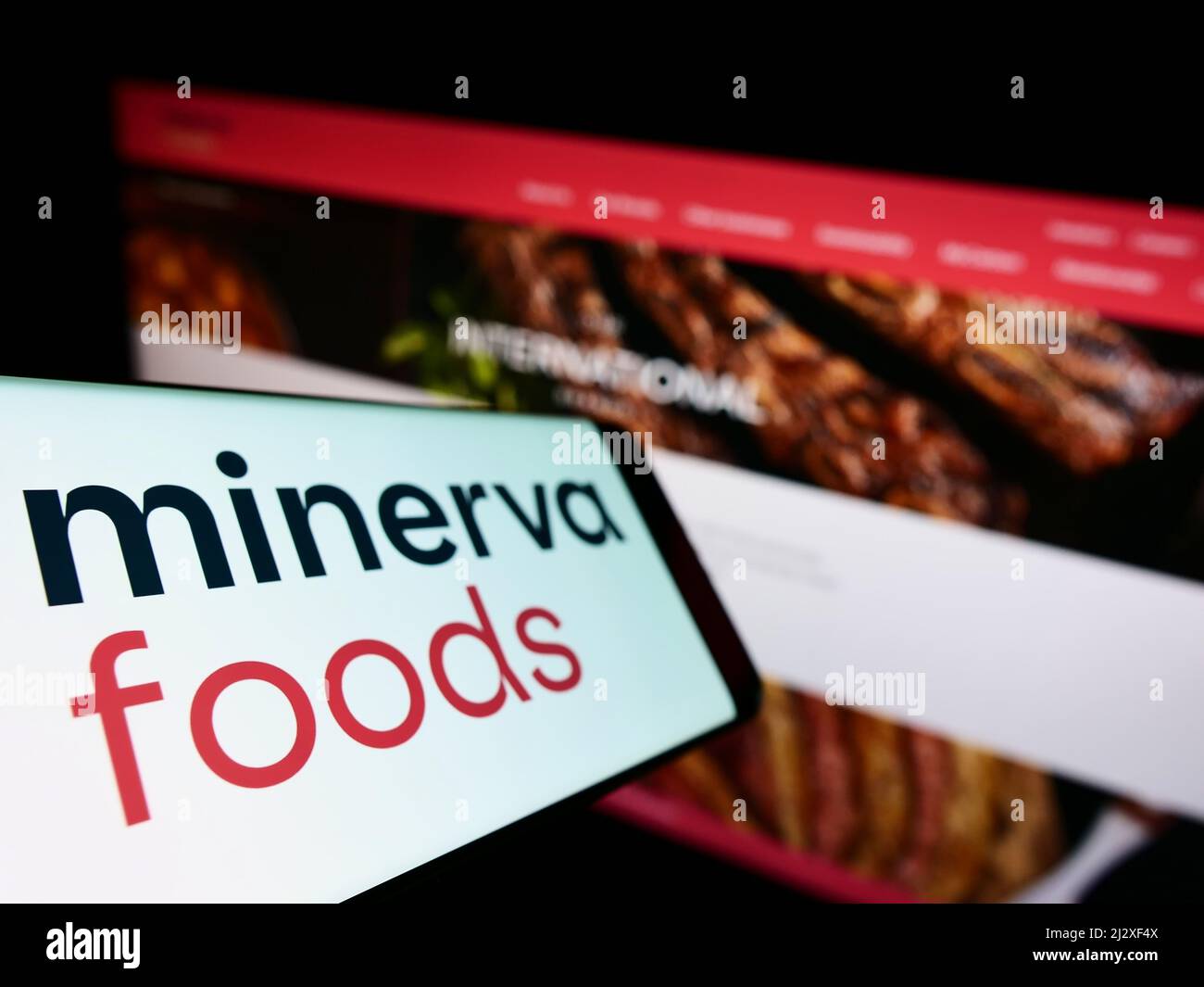 Cellphone with logo of Brazilian foods company Minerva S.A. on screen in front of business website. Focus on left of phone display. Stock Photo
