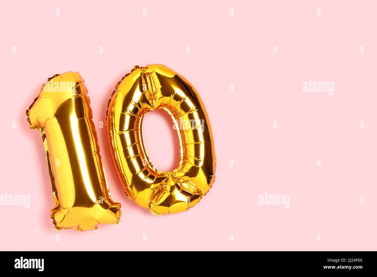 Number 10 golden balloons with copy space. Ten years anniversary celebration concept on a pink background. Stock Photo