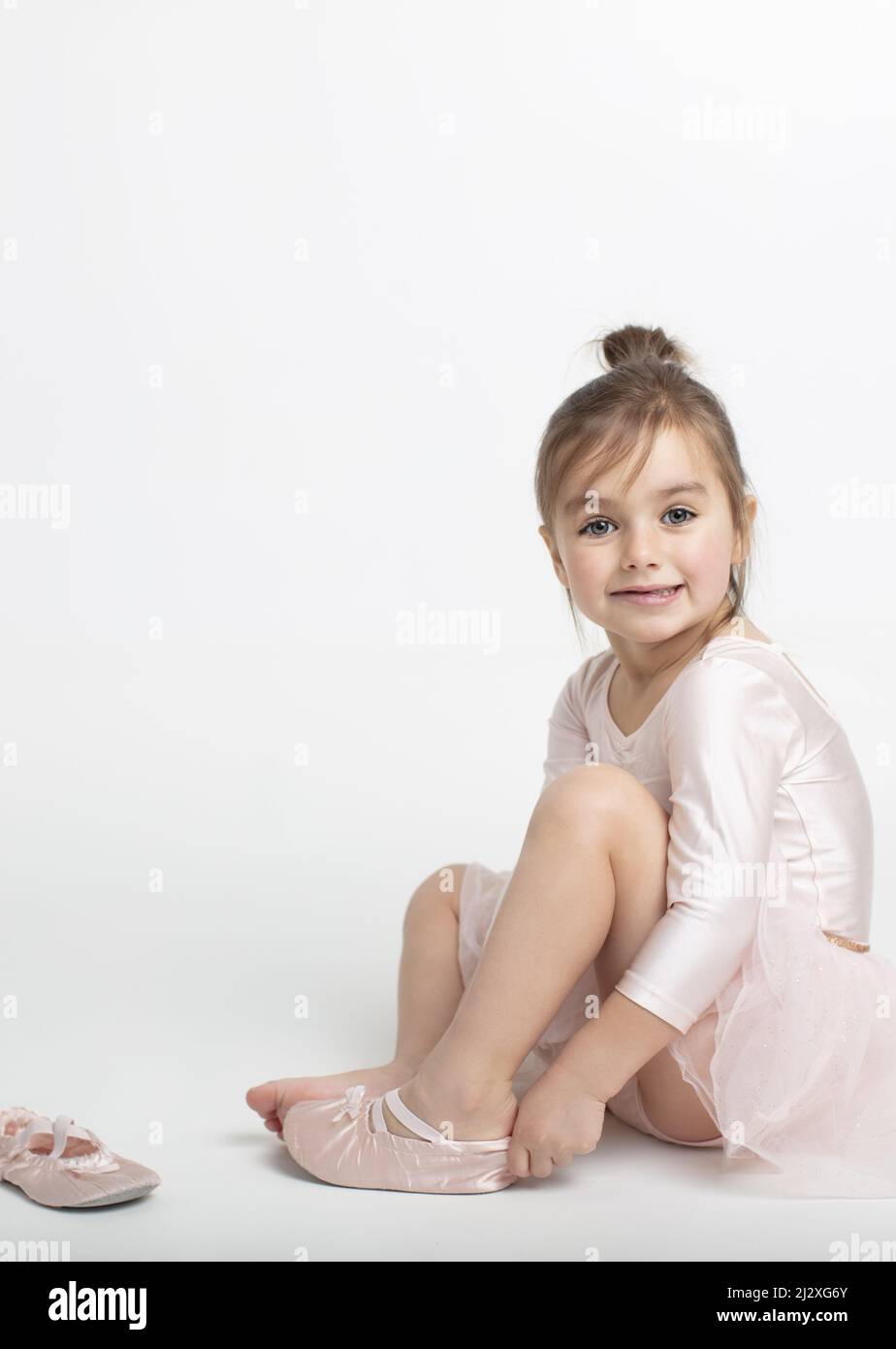 Toddler girl putting on her ballet shoes with the joy and excitement