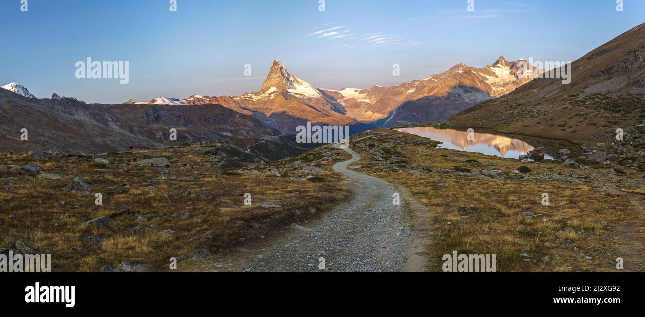 A hiking trail leading down from Fluhalp towards lake Stellisee with Mount Matterhorn in the days last light in the far distance. Wallis. Switzerland Stock Photo