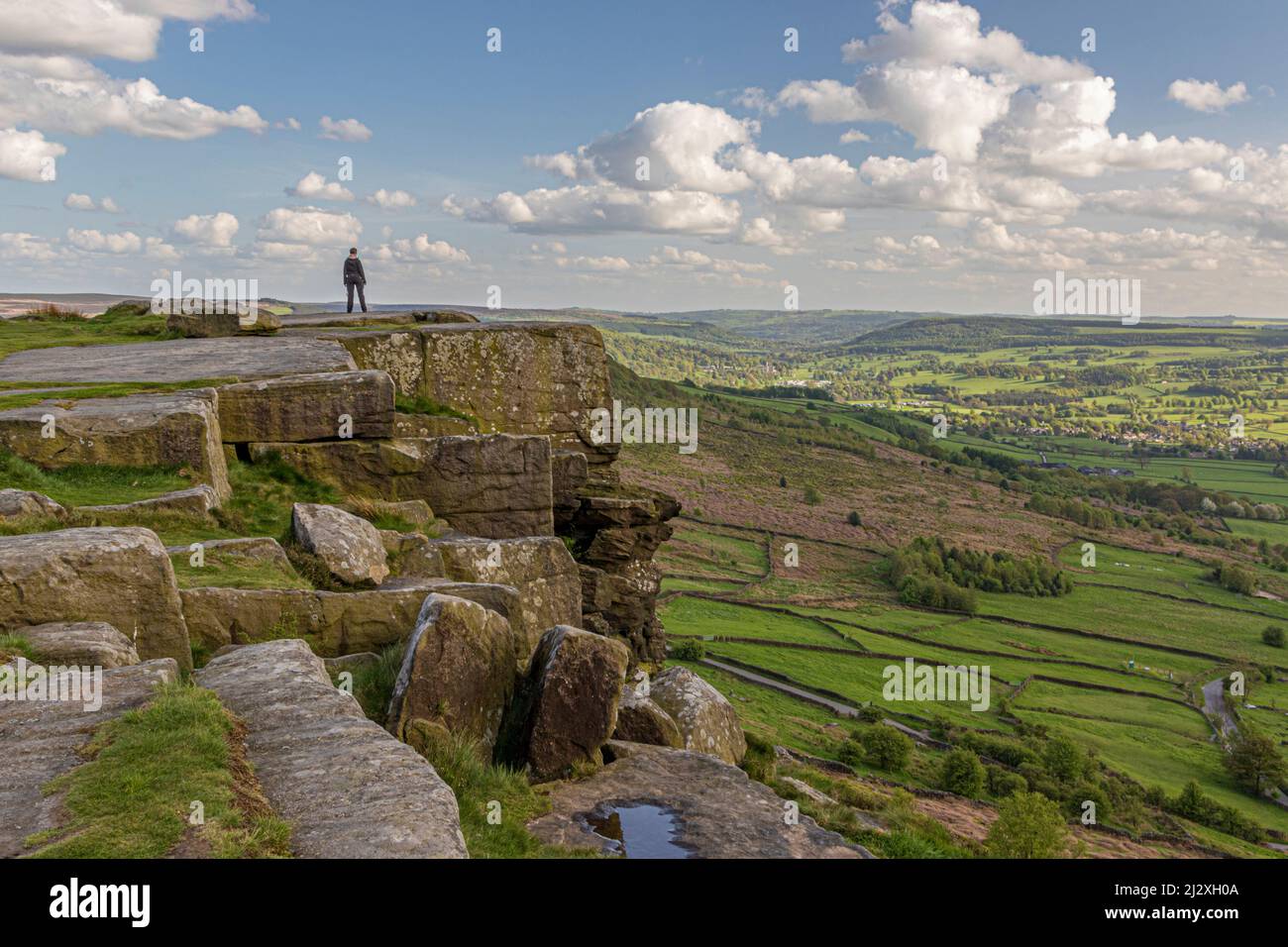 Person standing on cliff edge looking down valley at Curbar edge, Peak District, England, UK Stock Photo