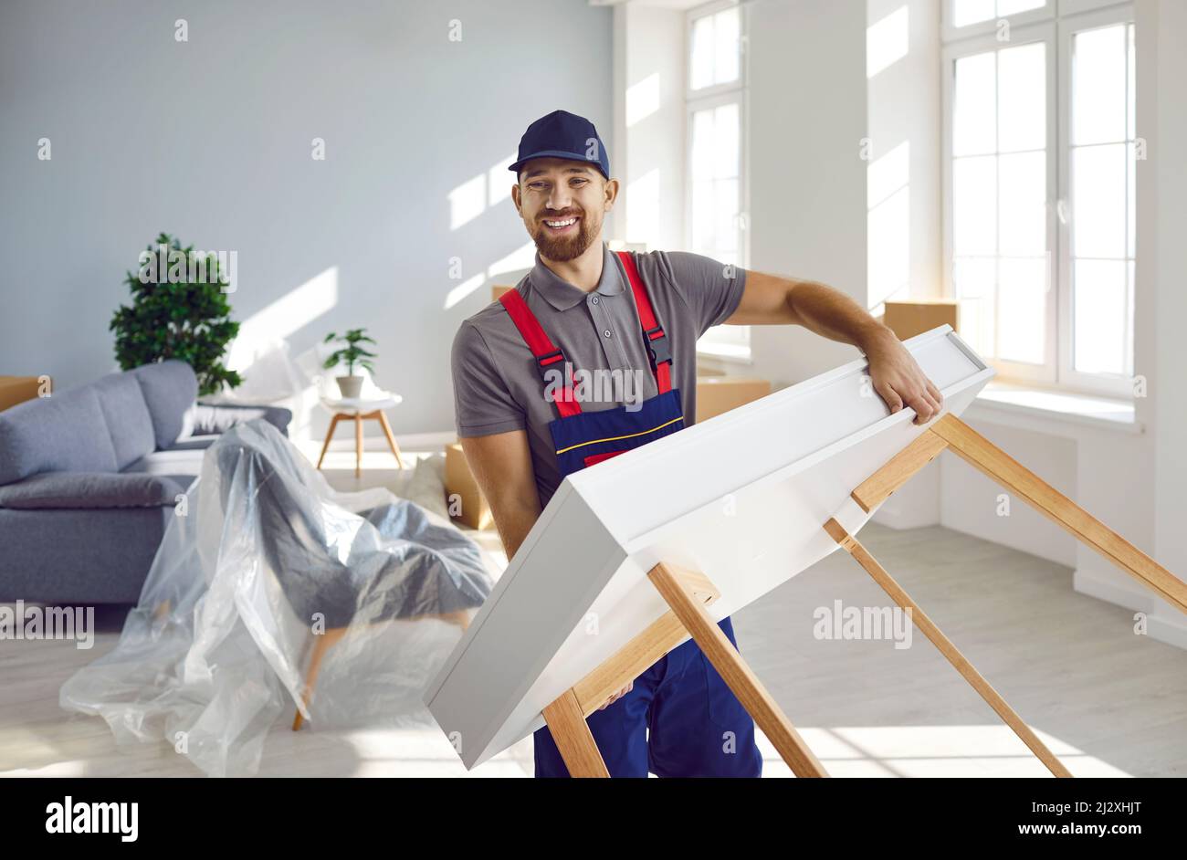 Happy young truck delivery or moving company worker carrying furniture and smiling Stock Photo