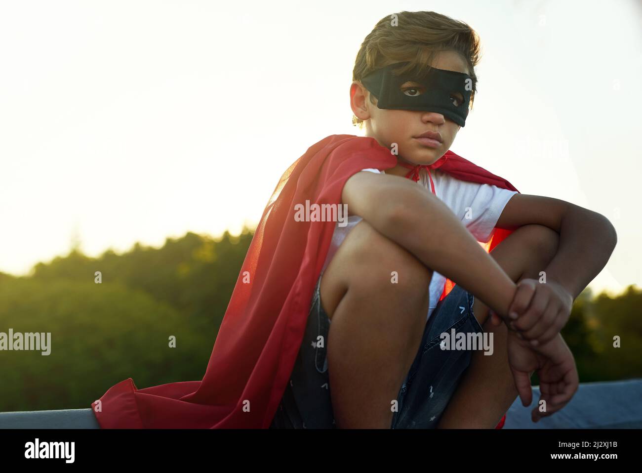 Watching over his neighbourhood. Shot of a young boy in a cape and mask playing superhero outside. Stock Photo