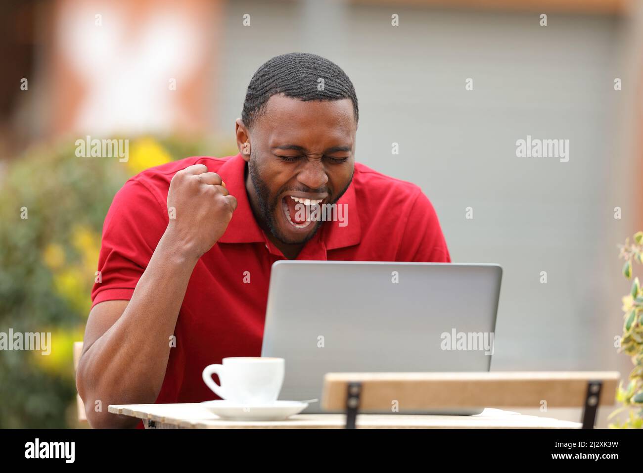 Excited man with black skin checking laptop content celebrating in a bar terrace Stock Photo