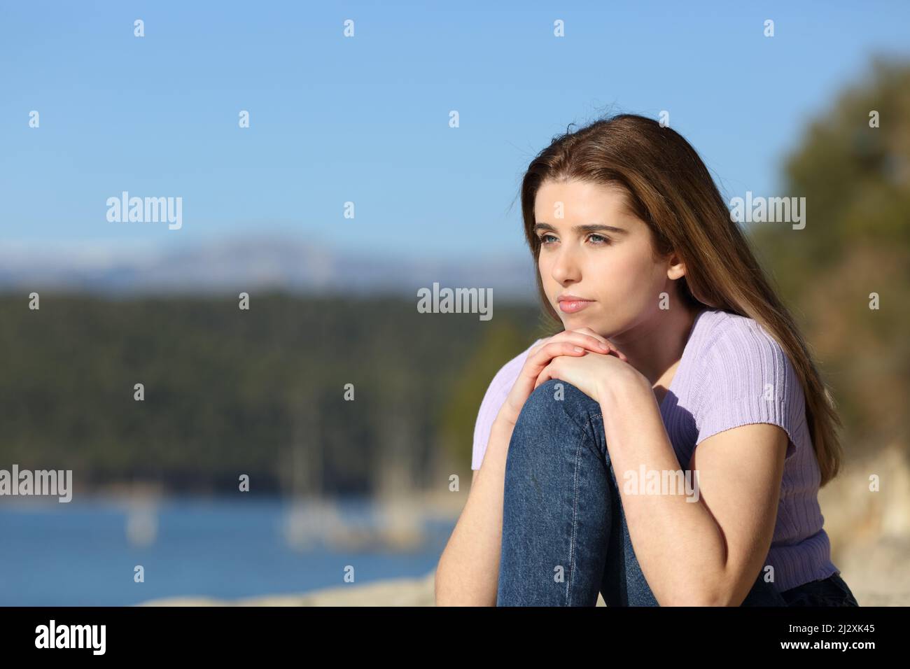 Pensive teen sitting contemplating beautiful views of a lake Stock Photo