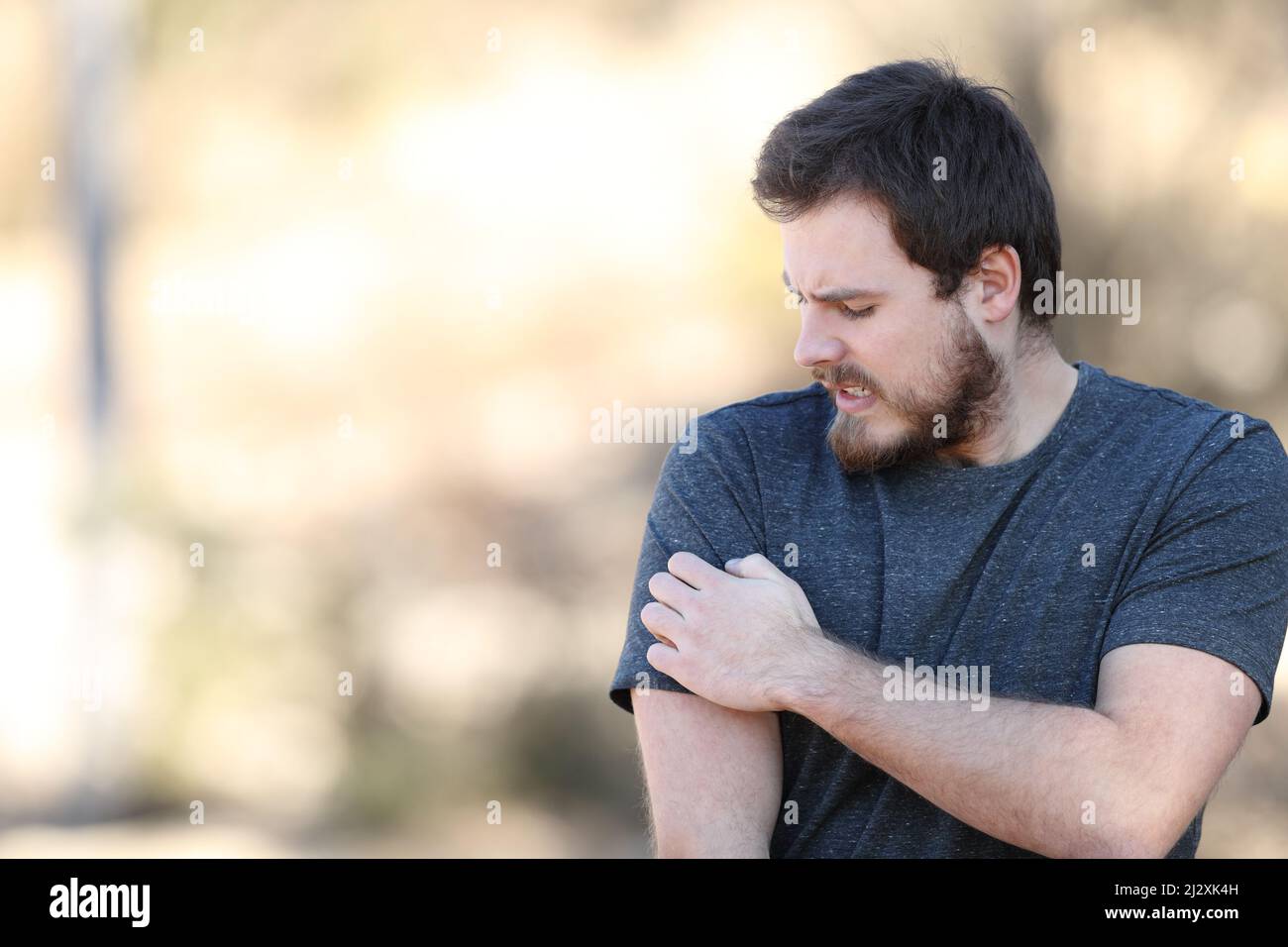 Stressed man scratching itchy arm complaining in nature Stock Photo