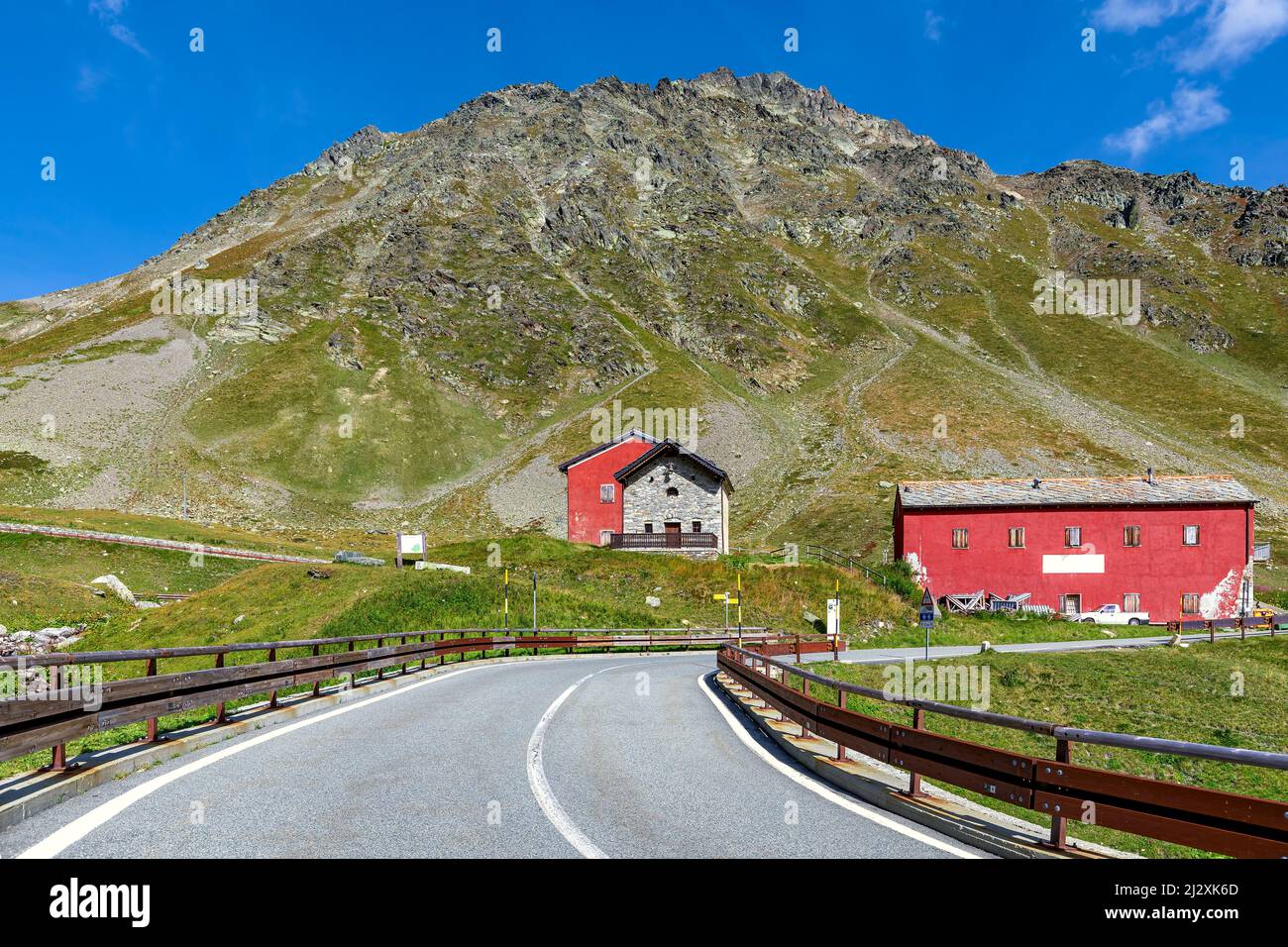 Road towards houses and mountain under blue sky on background at Great St Bernard Pass on the border between Italy and Switzerland. Stock Photo