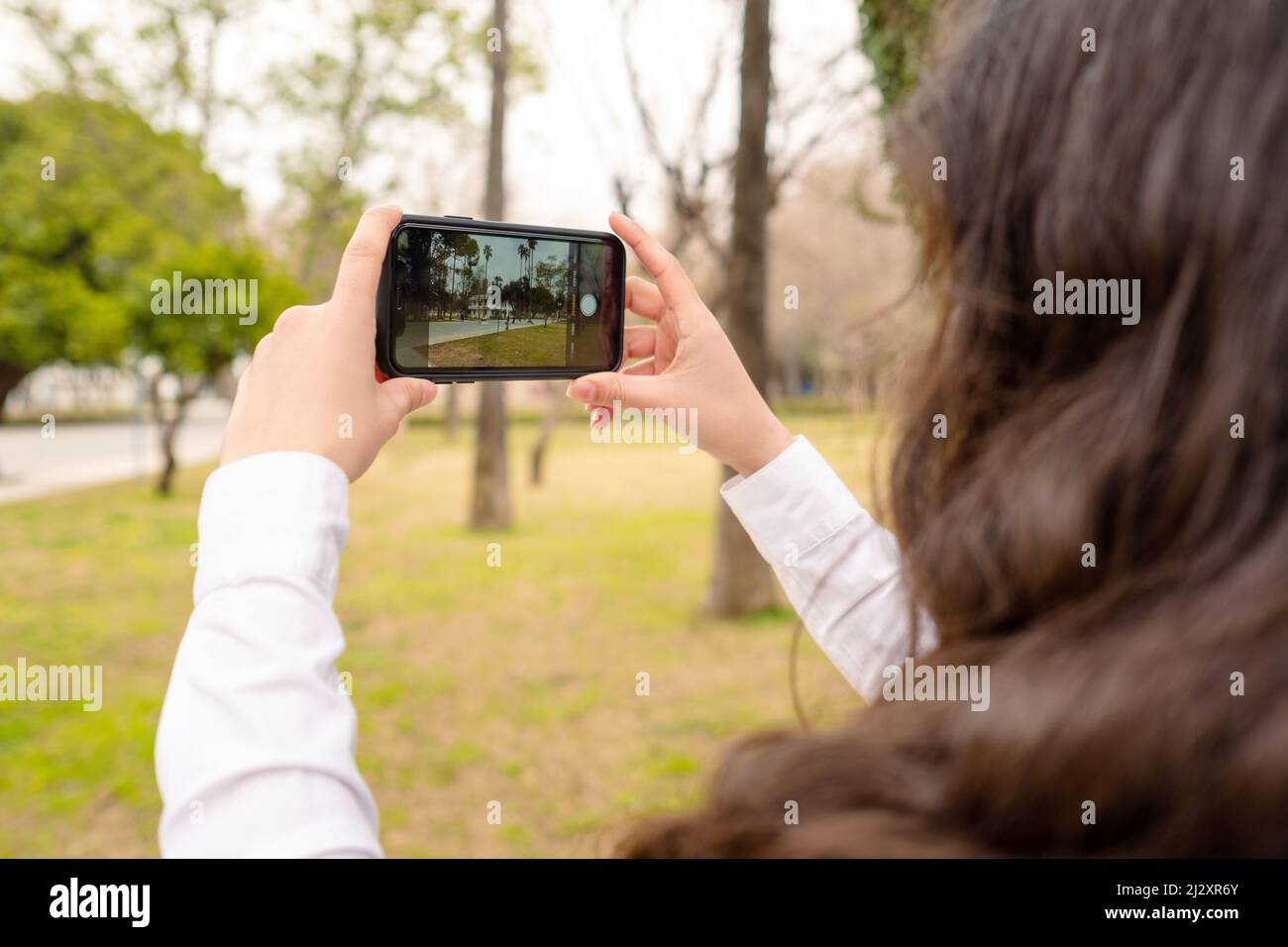 Taking photo, young woman takes a picture to immortalize a park scene, green park and smartphone Stock Photo