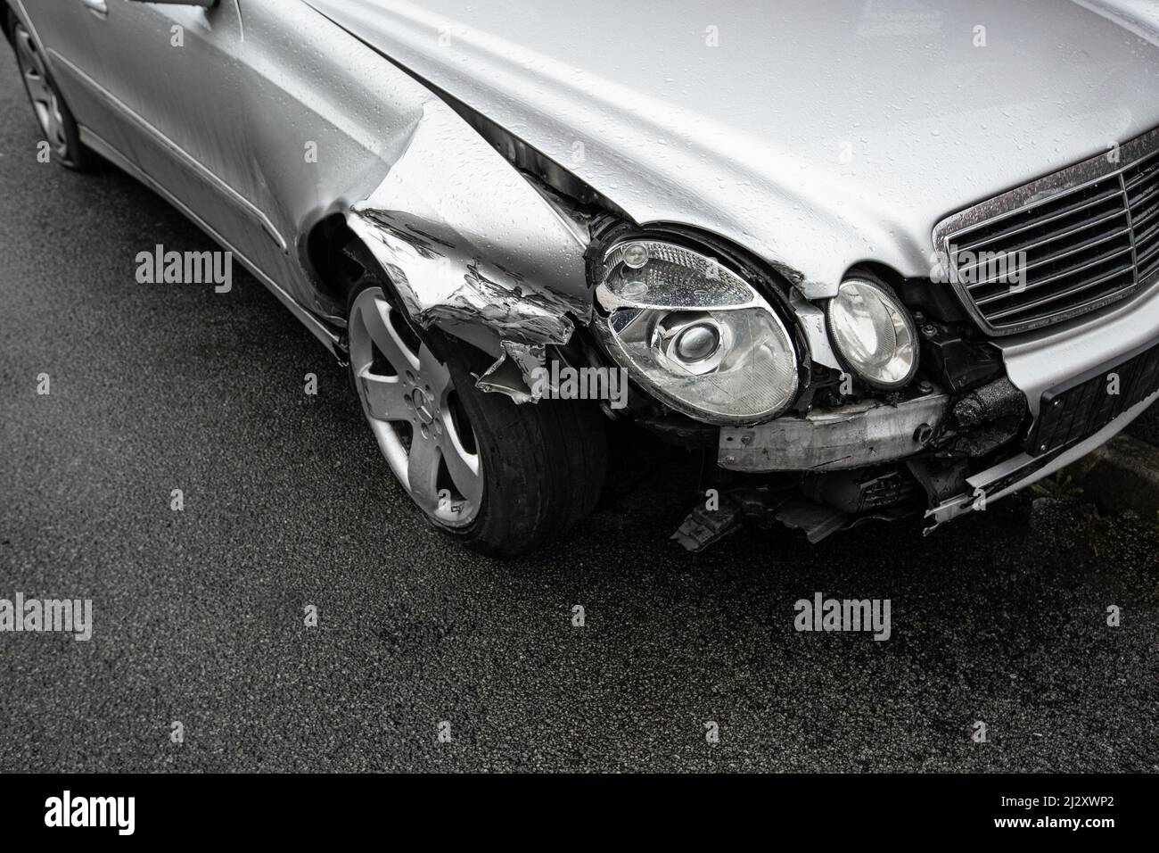 A close up of the damage to a silver car's front wing, wheel and headlights involved in a road traffic accident with copy space Stock Photo