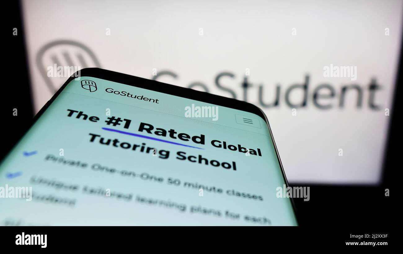 Smartphone with website of Austrian tutoring company GoStudent GmbH on screen in front of business logo. Focus on top-left of phone display. Stock Photo