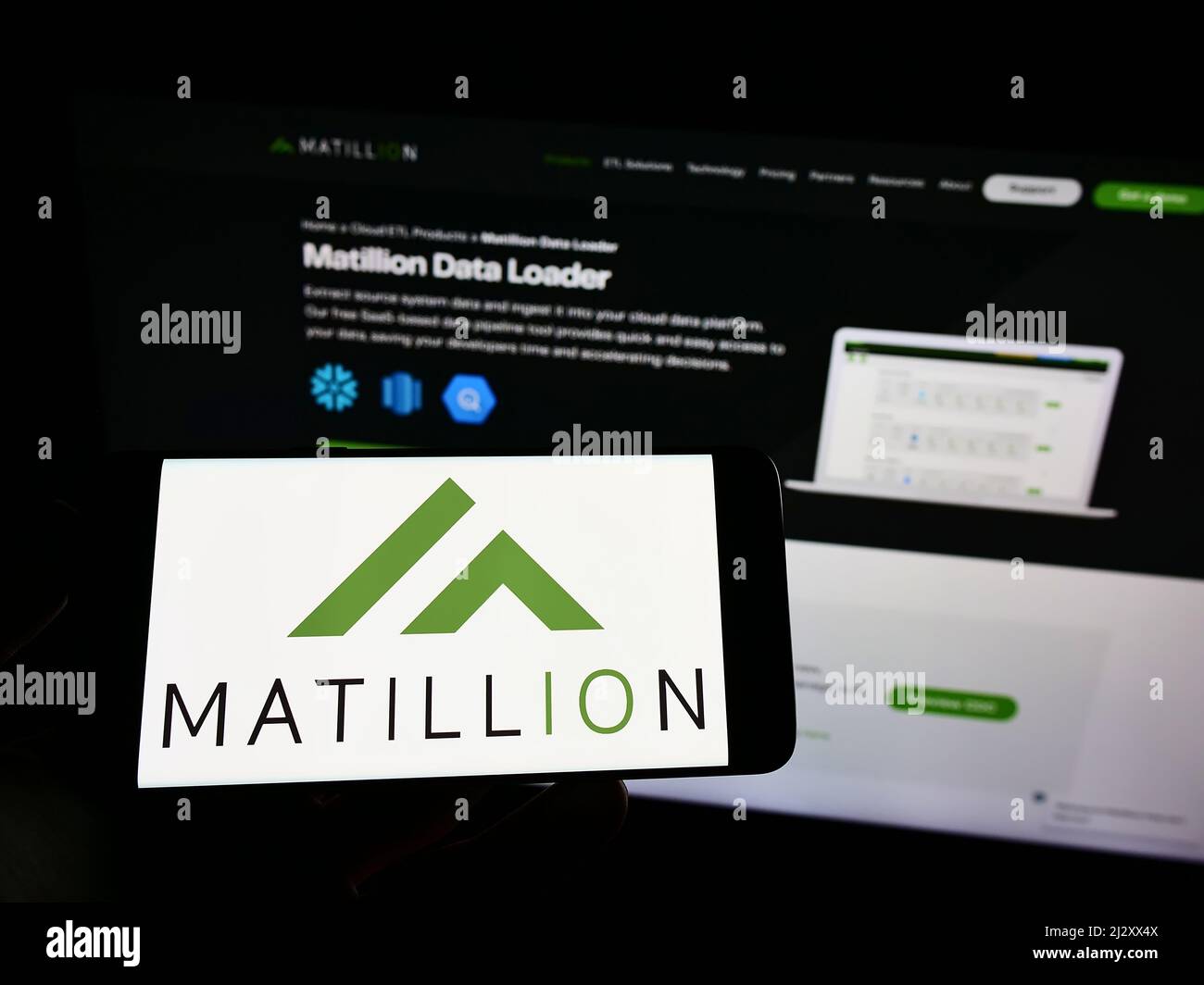 Person holding cellphone with logo of British software company Matillion Ltd. on screen in front of business webpage. Focus on phone display. Stock Photo