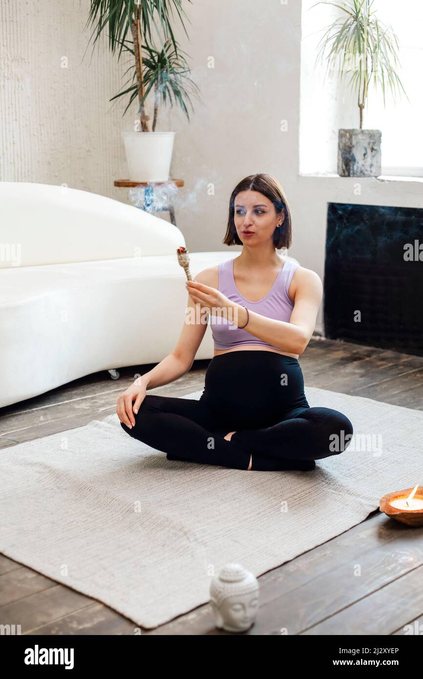 Calm pregnat female burning sage smudge stick and smelling smokein