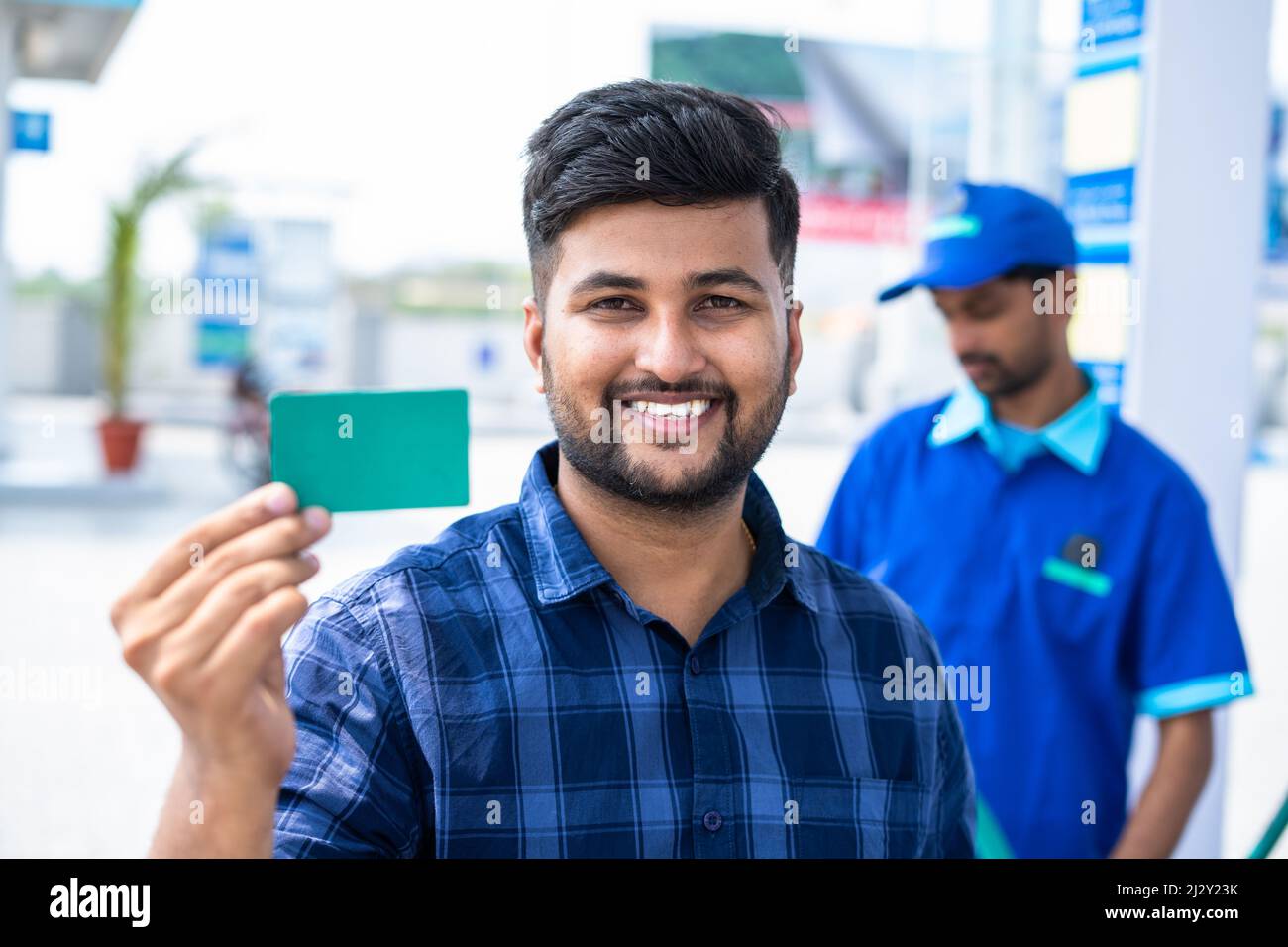 Smiling customers showing green empty card by looking camera at petrol pump - concept of employee id, offer on fuel card, promotion and advertisement. Stock Photo