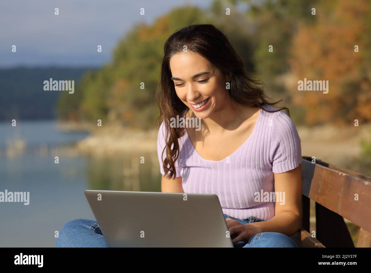 Happy woman using a laptop sitting in a lake on holiday a sunny day Stock Photo