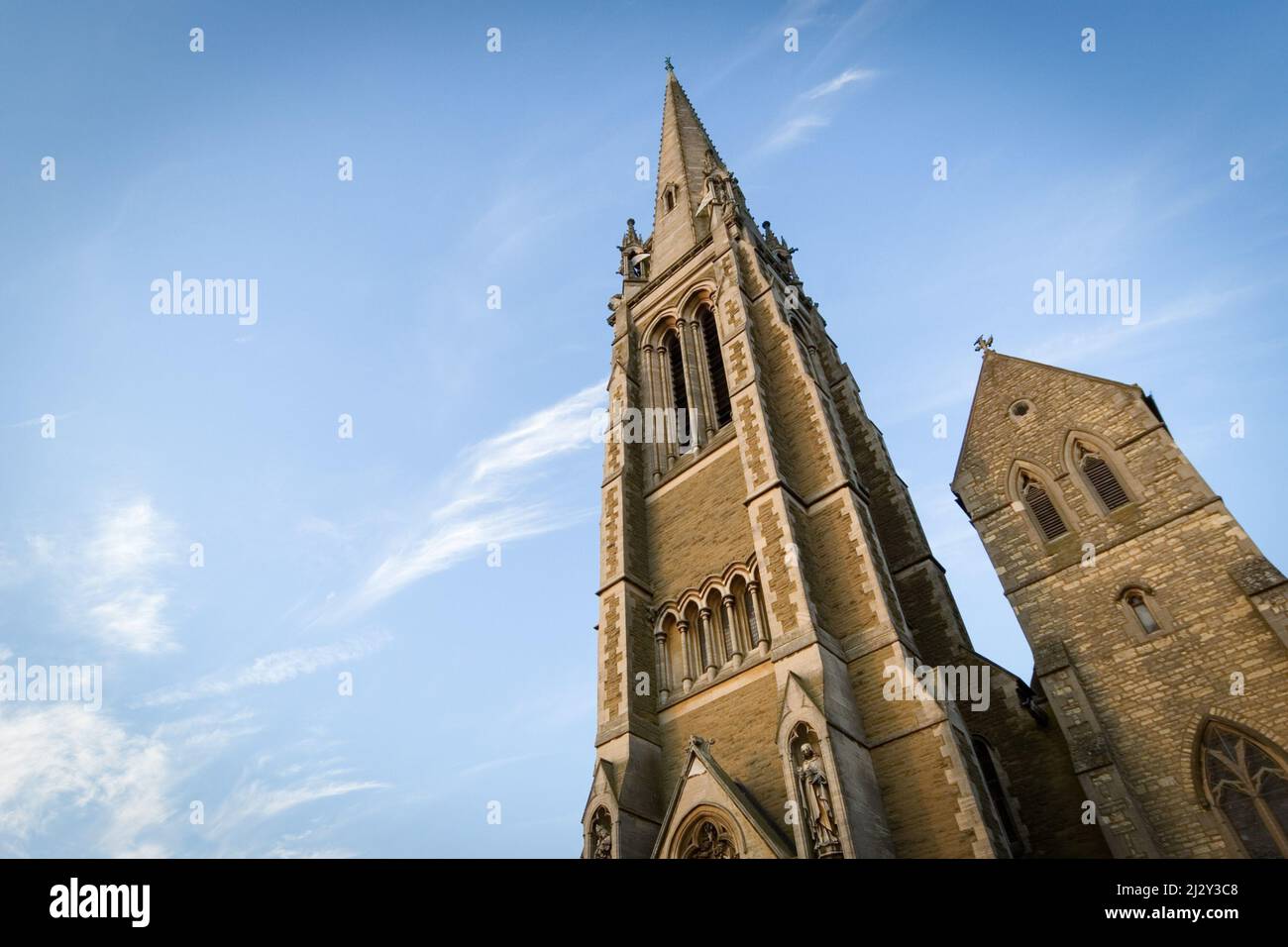 Traditional English Spired Church. A low, wide angle view up the spire of a Victorian stone built English church set against blue sky copy space. Stock Photo