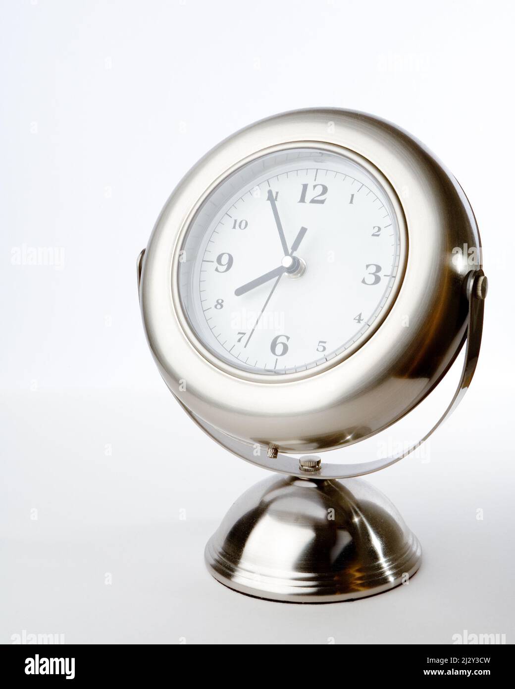 Silver clock. A brushed chrome clock on a stand showing the time approaching 4 o'clock. Studio lighting isolated on a white background. Stock Photo