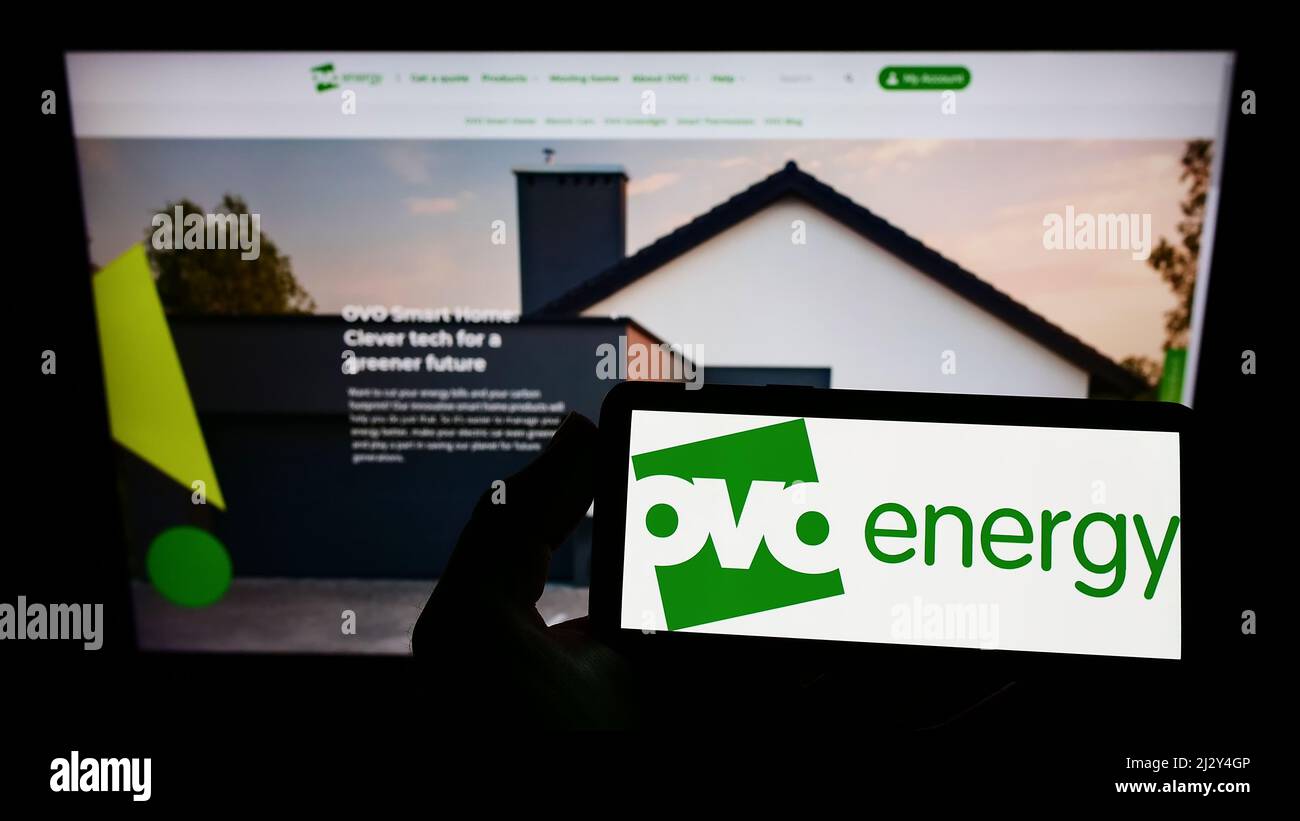 Person holding smartphone with logo of British utility company OVO Energy Ltd on screen in front of website. Focus on phone display. Stock Photo